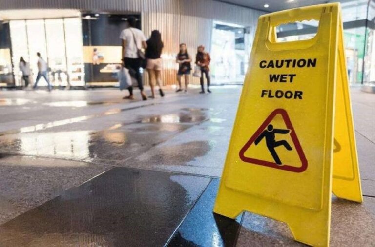 Señal amarilla de suelo mojado junto a un pavimento húmedo en un espacio interior